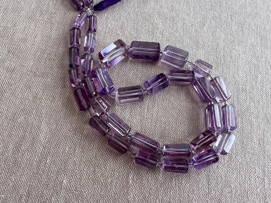 Close-up of Brazilian Amethyst cylinder beads showing rich purple color, excellent transparency, and sparkling faceted surfaces.