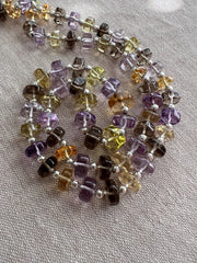 Close-up of AAA faceted button gemstone beads showing transparent purple, green, golden yellow, and lemon yellow colors.