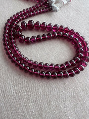 Close-up of transparent Rhodolite Garnet beads showing exceptional clarity, rich plum color, and beautifully polished smooth surfaces.