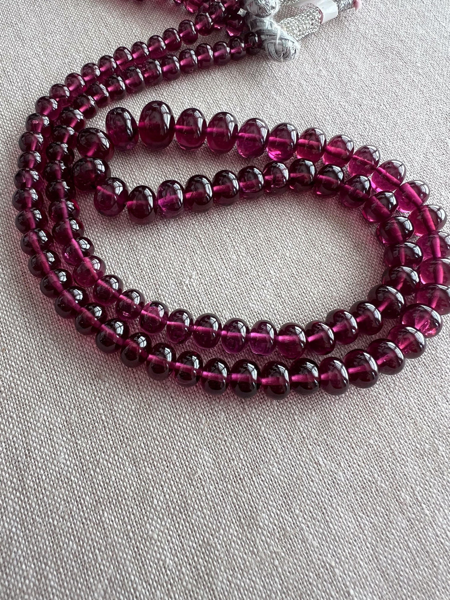 Close-up of transparent Rhodolite Garnet beads showing exceptional clarity, rich plum color, and beautifully polished smooth surfaces.