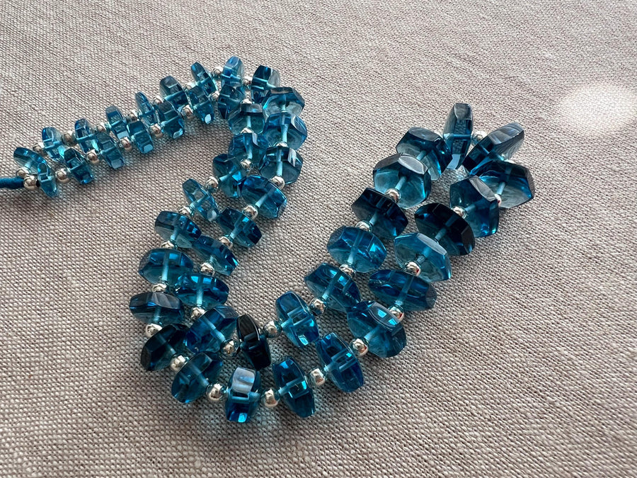 Close-up of Swiss Blue Topaz gemstone beads showing vibrant blue color, exceptional clarity, and sparkling faceted bolt cuts.