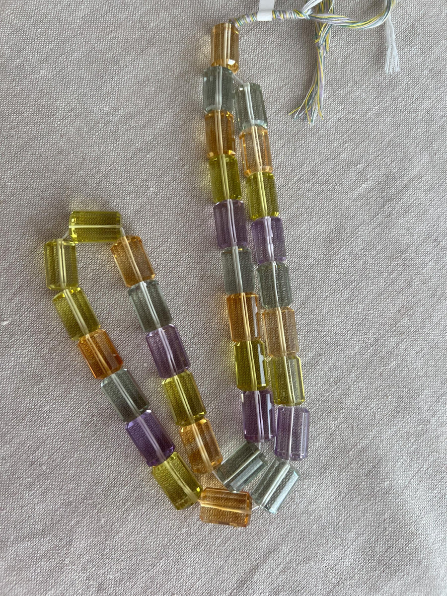 18-inch strand of mixed semi-precious faceted cylinder beads featuring 32 transparent gemstones in approximately 10x15mm sizes.