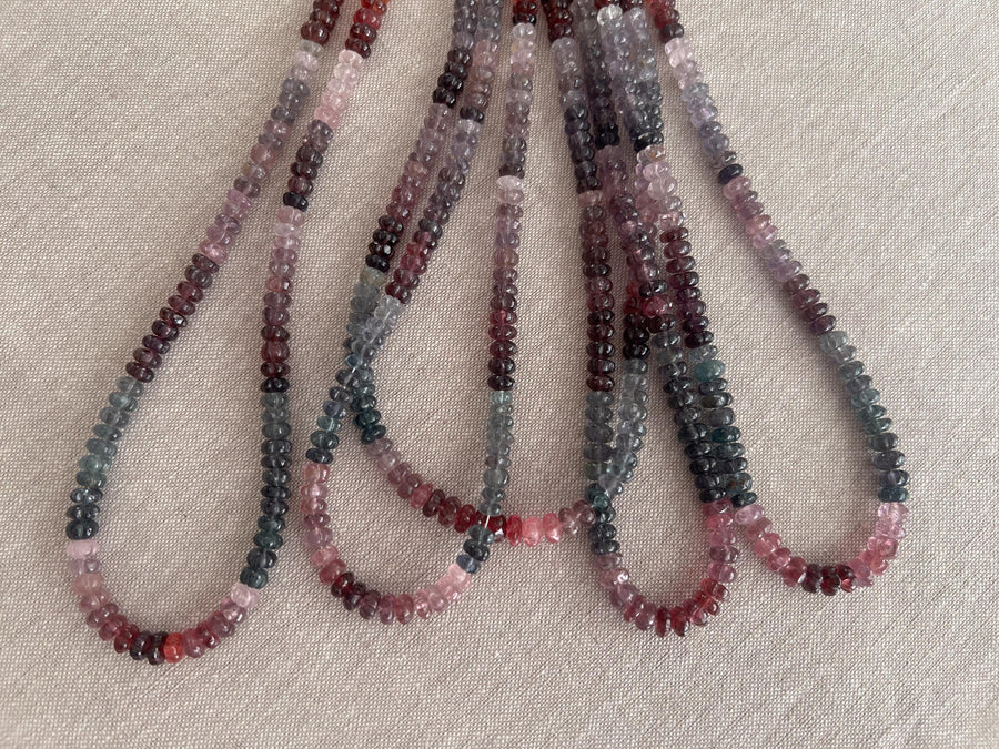 Close-up of AAA carved Spinel rondelle beads showing natural pink, red, and gray gemstone colors. multiple strands, 5 strands total