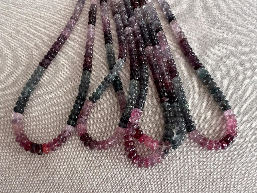 Close-up of AAA carved Spinel rondelle beads showing natural pink, red, and gray gemstone colors. multiple strands close up view